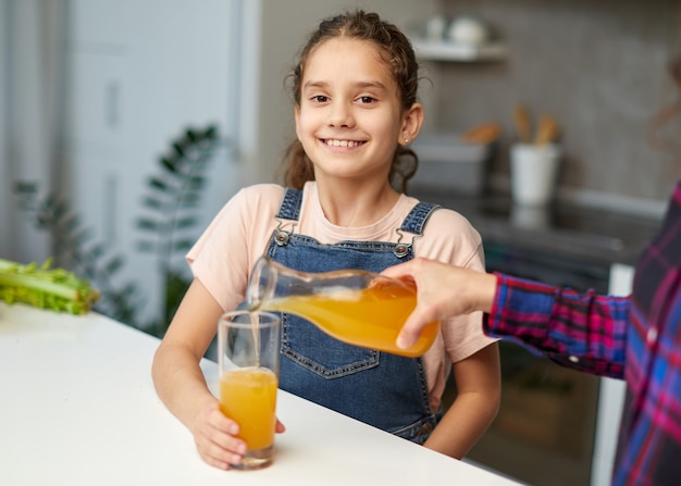 母親のイメージは、朝食に彼女のかわいい笑い娘オレンジジュースを注ぐ。