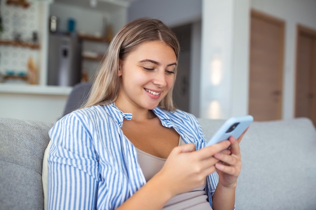 Image of nice young serious woman using mobile phone and thinking while sitting on sofa at living room