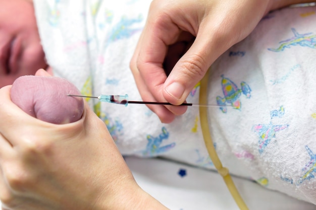 看護師の手の画像は、赤ちゃんの手に徐々に刺すような医療用針を使用して血液検査を行います。