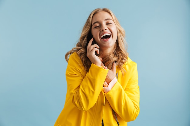 Фото Изображение радостной женщины 20-х годов в желтом плаще, смеющейся во время разговора по мобильному телефону
