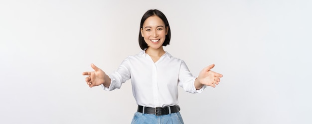 白い背景の上に立って挨拶する開いた手を伸ばしてゲストの実業家を歓迎する笑顔のアジアの女性の画像