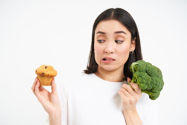 写真 ベジタリアンの女の子の画像は、ペストリーがブロッコリーにくっつくことを避け、白いカップケーキの代わりに野菜を食べています