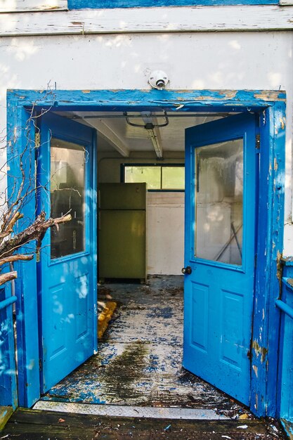 Image of Old abandoned blue double doors leading into a dilapidated room with white floors and walls