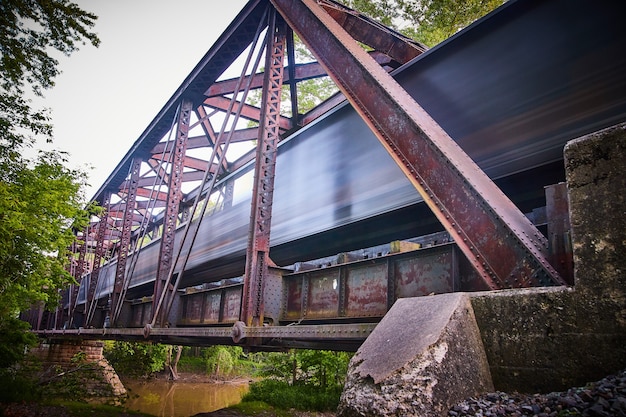 Image of Old metal train track bridge over river with blur of train crossing