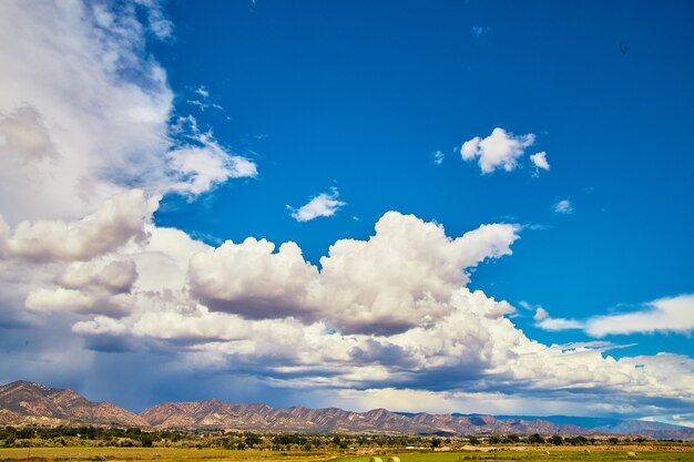 Image of Open blue sky with storm clouds entering against desert mountains along horizon