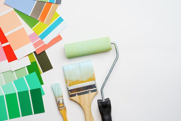 Image of palette with blue and green colors, roller, brushes on blank white background