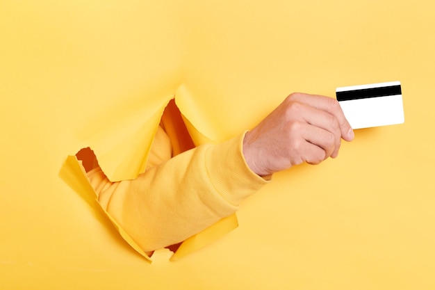 Image of person hand breaking through yellow paper and holding credit card recommend bank or shopping discounts earning money banking