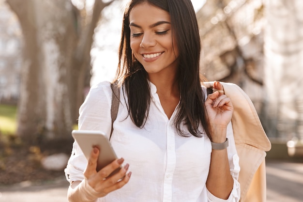 Image of Pleased brunette woman in shirt standing outdoors