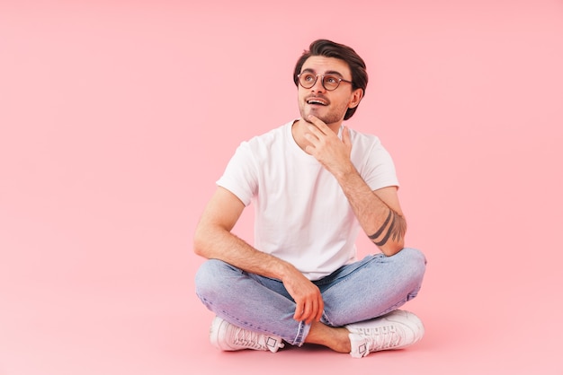 Photo image of pleased man wearing eyeglasses looking at copyspace while sitting with legs crossed isolated