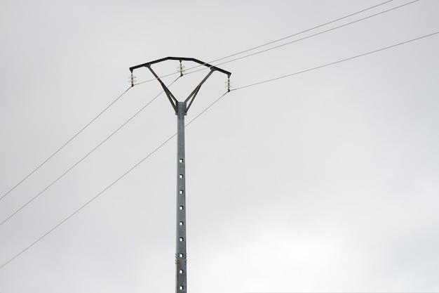 灰色の曇り空を背景にした電柱送電線の画像