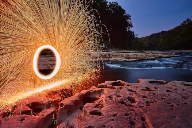 Image of Portal of yellow sparks against craggy stone and rock in front of waterfalls at Cataract Falls