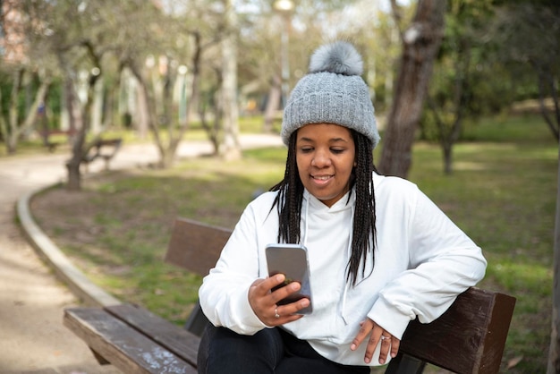 Image of positive african woman sitting park on a grass and using mobile phone