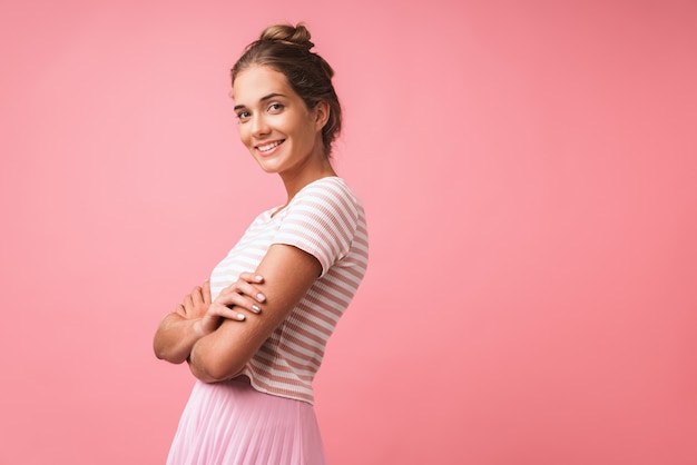 Image of positive beautiful woman wearing striped clothes smiling and standing with arms crossed isolated over pink wall