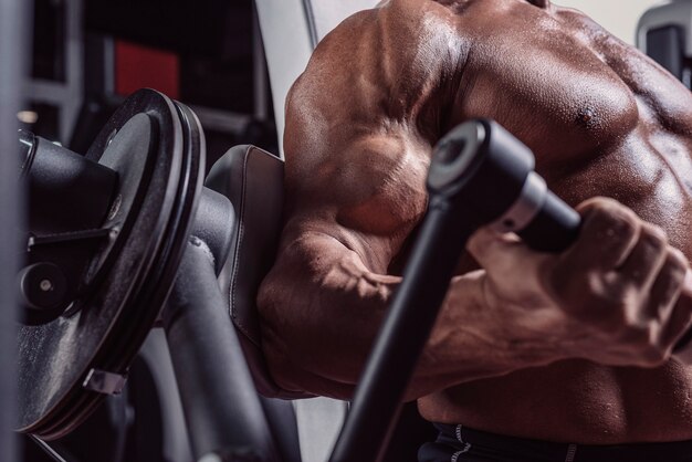 Image of a powerful athlete sitting on a bench in a gym and\
pumping biceps. fitness and bodybuilding concept. mixed media