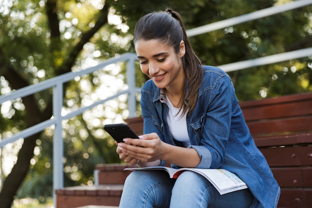 Foto immagine di giovane donna caucasica allegra abbastanza felice che si siede all'aperto che chiacchiera dal telefono cellulare.