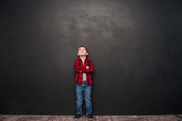 Image of pretty little boy standing over chalkboard and looking up