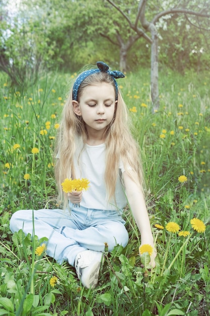 Image of pretty little girl sitting on dandelions field