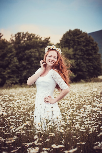 Image of pretty woman lying down on chamomile field, happy female holding in hand beautiful white flower, cheerful girl resting on daisy meadow, relaxation outdoor in springtime, vacation concept