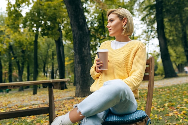 Image of pretty young woman drinking coffee at terrace cafetaria in the park Female in the city street drinking hot cappuccino looking at camera Pretty girl with cup of coffee Coffee on the go