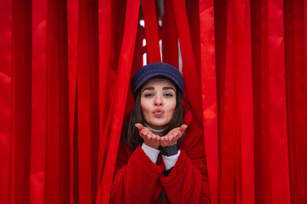 Image of a pretty young woman looks out between red curtain.