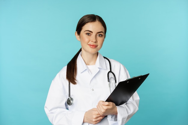 Foto immagine di dottoressa professionista, medico con la scrittura negli appunti, paziente in ascolto all'appuntamento della clinica ospedaliera, in piedi su sfondo turchese