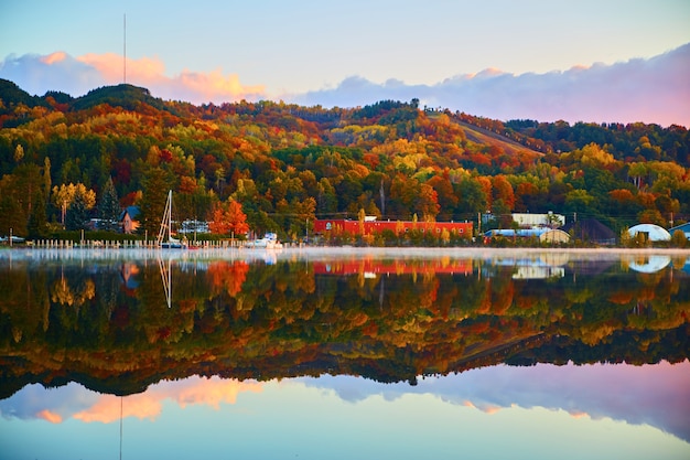 Image of Quaint village against a still as glass river of water with fall tress of orange, yellow, red and green