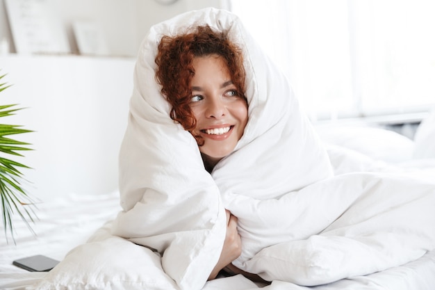 Photo image of a redhead pleased cheerful happy young lady in lingerie indoors in home hotel lies in comfortable bed.