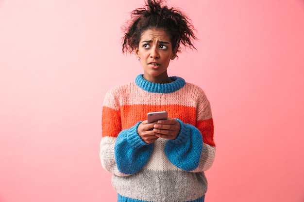 Image of a sad beautiful young african woman posing isolated using mobile phone.