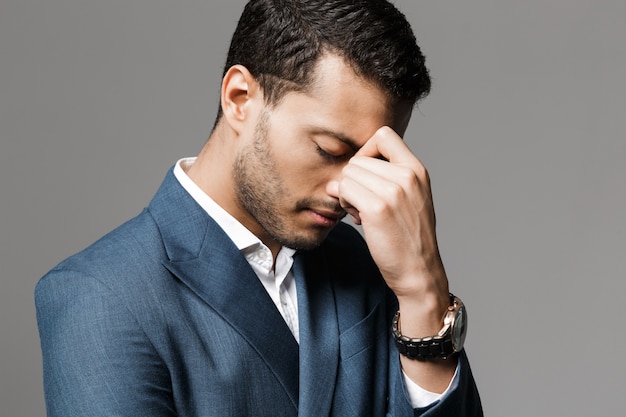 Image of a sad tired business man with headache posing isolated over grey wall wall.