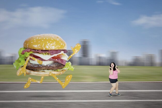 Foto immagine di una donna obesa spaventata che fugge da un hamburger mentre corre sulla pista