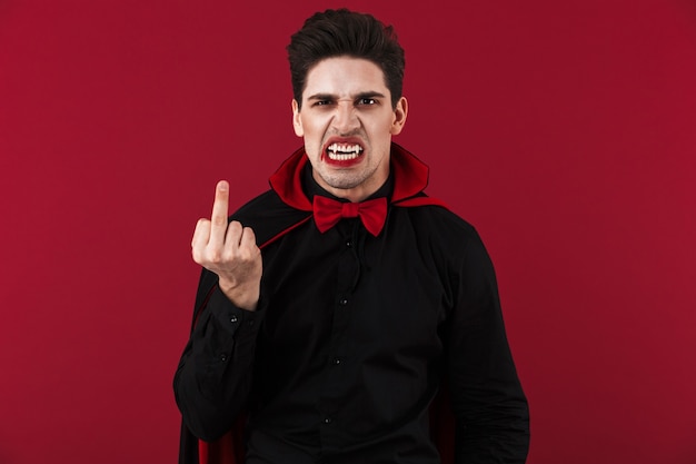 Photo image of scary vampire man with blood and fangs in black halloween costume showing middle finger