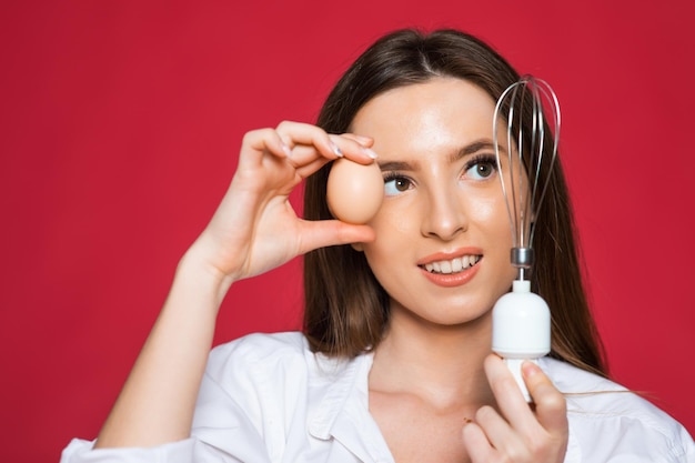 Image of screaming excited positive young woman chef holding whisk and eggs isolated