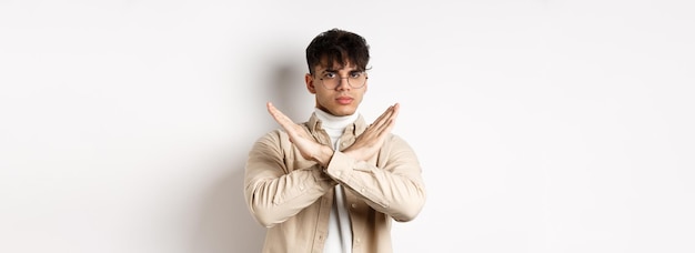 Image of serious young guy in glasses say no showing cross gesture make stop sign to disagree or pro