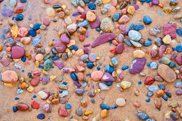 Image of Shiny red, black, blue, pink and purple multicolored stones against a sandy shore