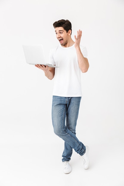 Immagine del giovane eccitato scioccato in posa isolato su un muro bianco utilizzando il computer portatile.