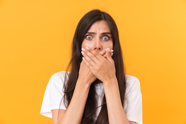 Image of shocked scared woman with long hair covering her mouth with fear isolated over yellow wall