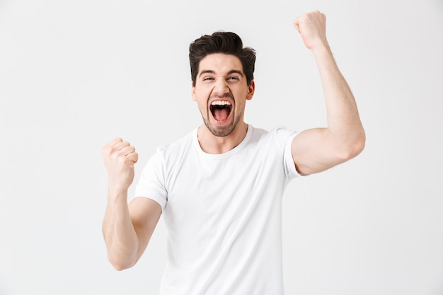 Image of a shocked surprised excited happy young man posing isolated over white wall  make winner gesture.