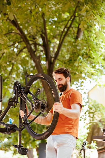 Image showing enthusiastic sporty caucasian man gripping and examining damaged dismantled bicycle wheel for repair. Healthy young active male cyclist reattaching bike tire rubber.