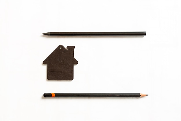 Image of small black model of a house with black pencils on a white background