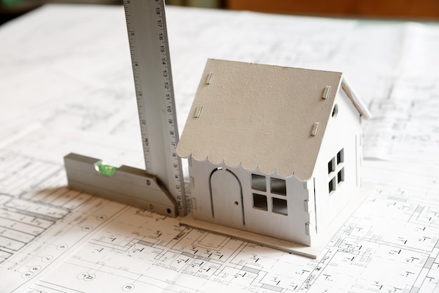 통치자가 있는 건축 청사진 계획에 있는 작은 흰색 장난감 모델 하우스의 이미지. 건축가 작업 개념