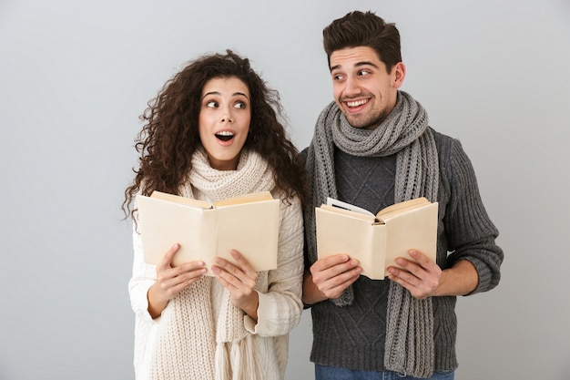 Image of smart man and woman reading books together, isolated over gray wall