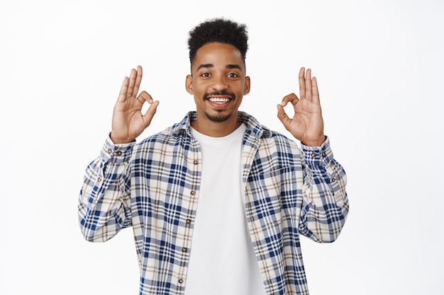 Image of smiling african american guy 20s showing okay, OK zero gesture and nod in approval, say yes, positive feedback, like and agree with you, praise choice, standing over white background