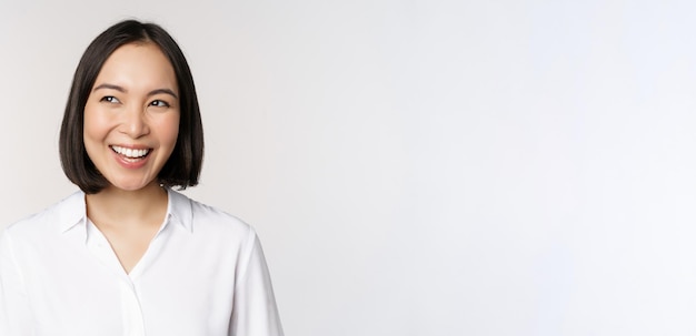 Image of smiling asian woman planning thinking of smth daydreaming standing over white background with smug face