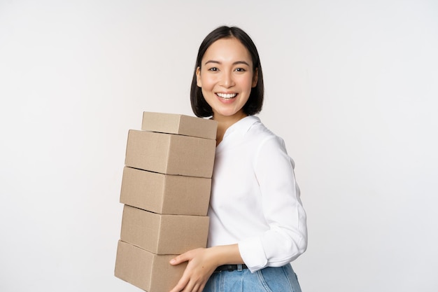 Image of smiling happy asian woman holding pile of boxes concept of delivery shopping or business white background