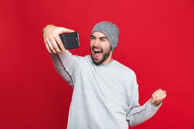 Image of smiling man 30s holding smartphone and taking selfie photo, isolated