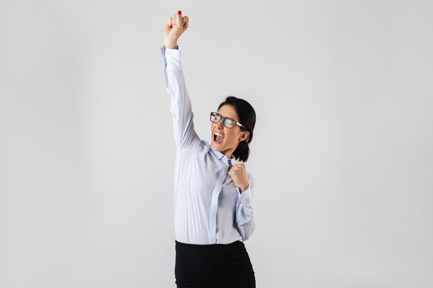 Image of smiling secretary woman wearing eyeglasses standing in the office, isolated over white wall