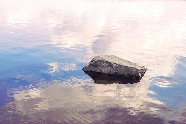 Foto immagine di una pietra nell'acqua e il riflesso del cielo serale