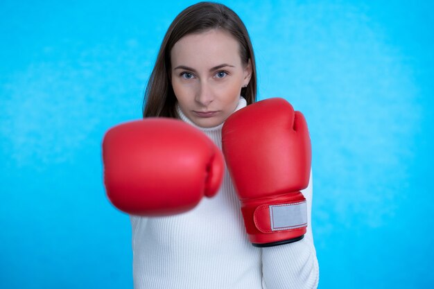 Image strong young woman boxer posing isolated over blue wall wall wearing boxing glove.