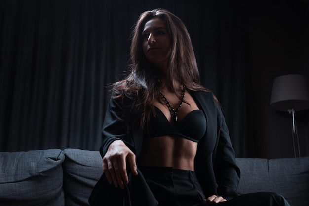 Image of a stylish beautiful brunette sitting on a sofa. Business suit and sexy underwear. Mixed media