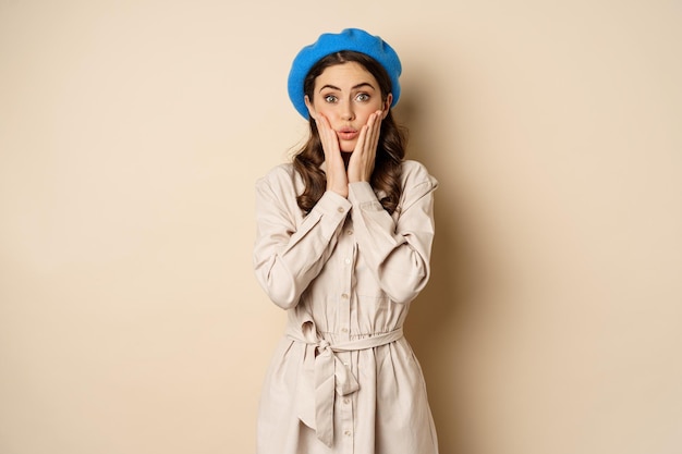 Image of stylsh beautiful woman looking surprised shocked reaction at camera posing in trench coat a...